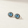 Gemstone stud earrings with blue oval center and silver beaded halo