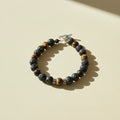 Beaded talisman bracelet with dark stone beads, brown-gold accents, and silver clasp
