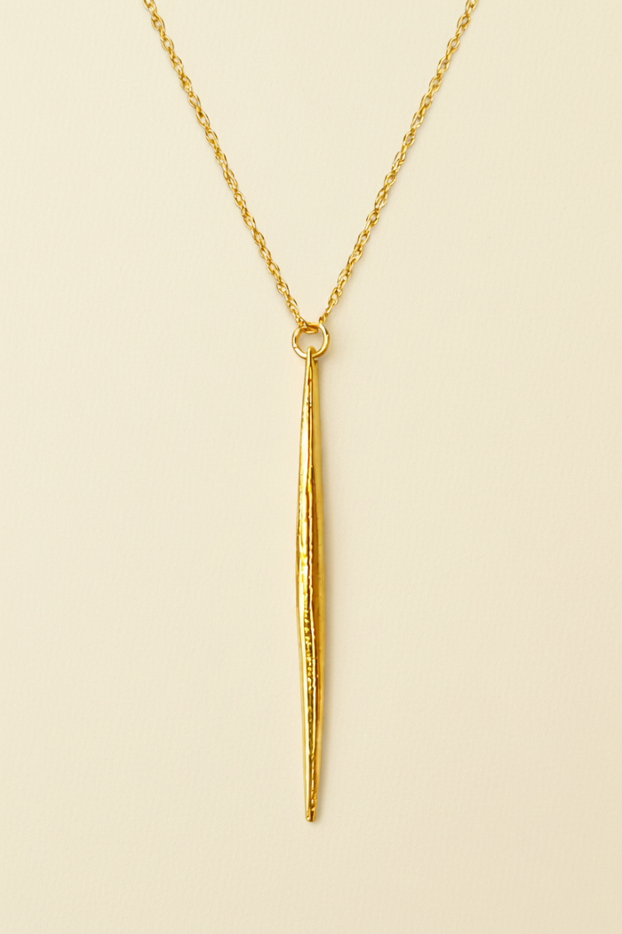 Gold necklace with a long, thin pendant on a white background