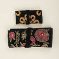 Black jewelry roll with gold floral embroidery; pink flower accents, rolled and tied.