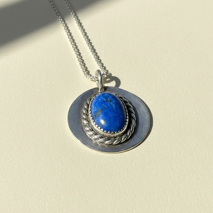 Silver-tone pendant necklace with blue oval gemstone set in braided rope bezel