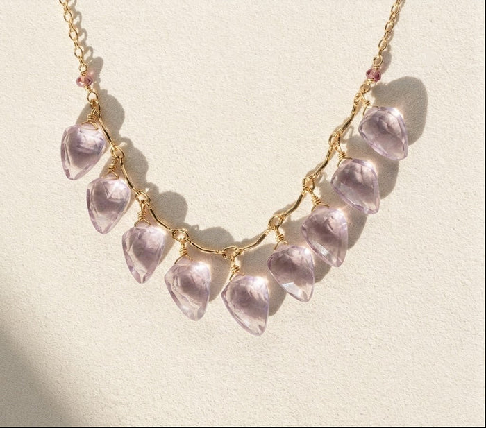Gold-tone necklace with lilac petal-shaped charms in a curved row