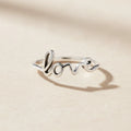 Silver-toned Love script ring with raised cursive lettering and heart dot