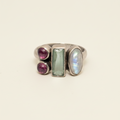 Multi-stone ring with two round purple stones, rectangular green center, and iridescent oval