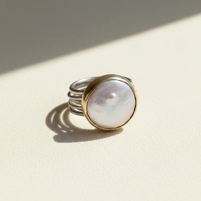 Nomad dancing pearl ring with opalescent round pearl, silver band, and gold bezel