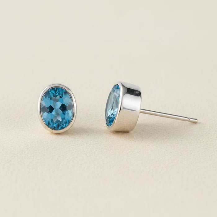 Oval blue gemstone stud earrings with silver bezel and post backing.
