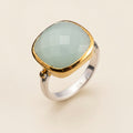 Ring with gold and silver band and light green stone on a white background