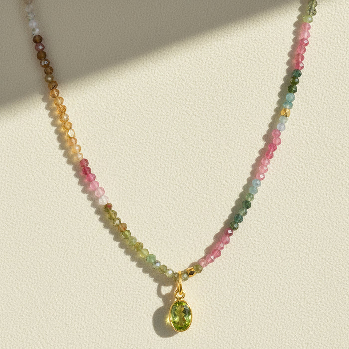 Multicolor beaded charm necklace with gold clasp and green teardrop pendant.